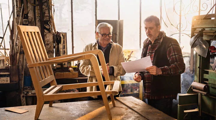 Two craftsmen in their workshop working on an armchair frame A person sitting on a wooden table