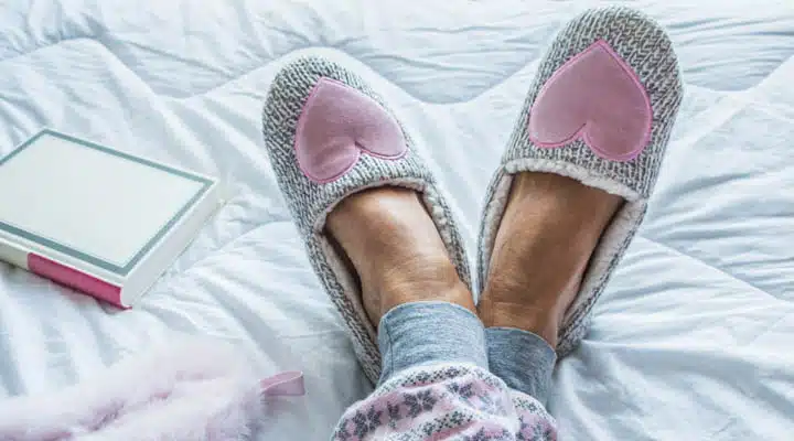 Close Up of Senior Woman Legs in Fluffy Slippers on the Bed Una persona sentada en una cama