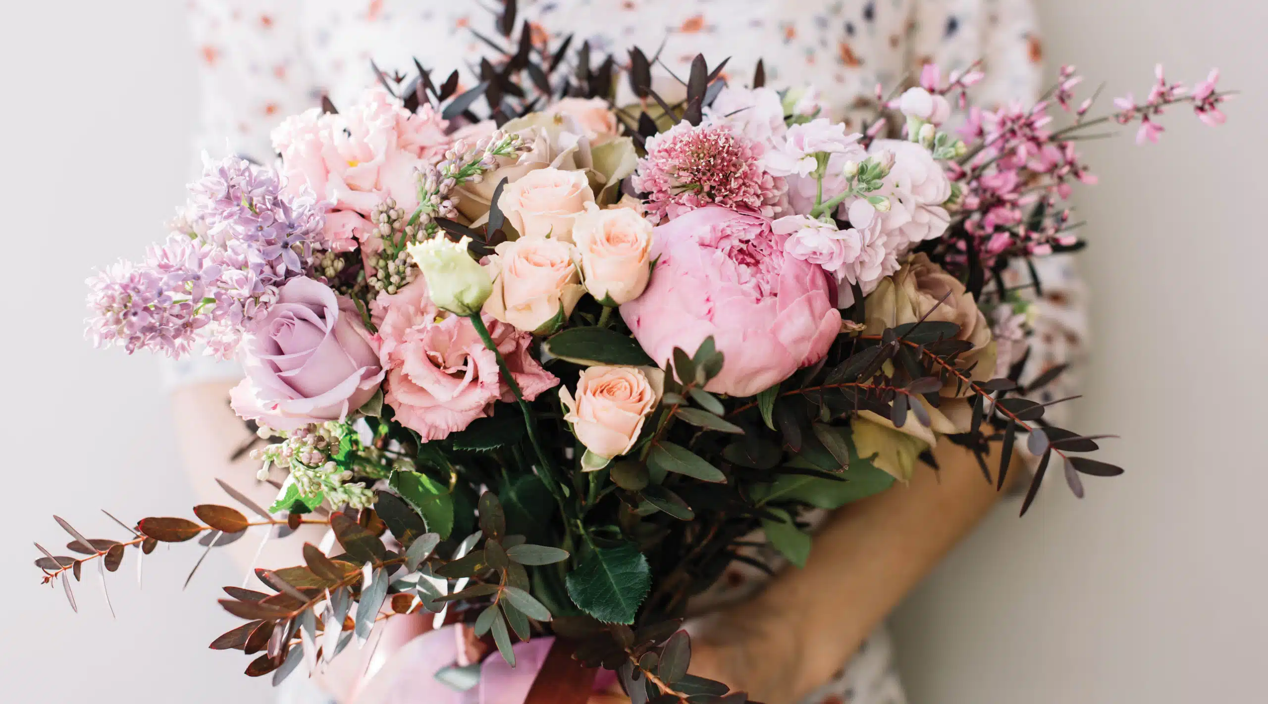 Florist woman holding a beautiful fresh blossoming flower bouquet of peony, roses, lilac, eustoma, mattiola in pink and lavender colors on the grey wall background A close up of a flower