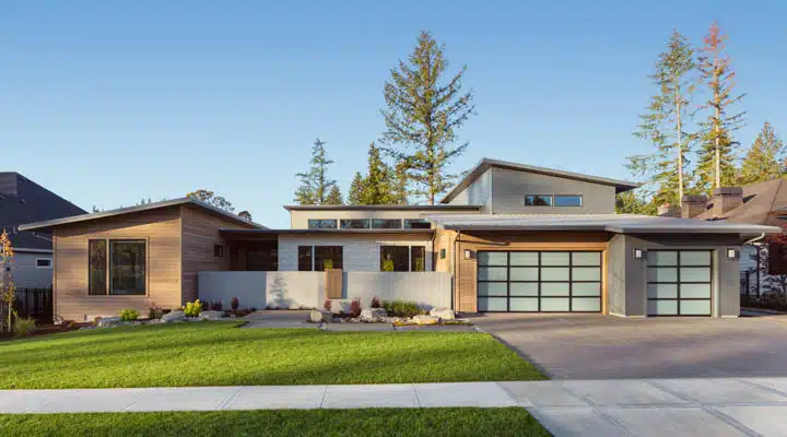 Contemporary home exterior in late afternoon. Features three car A large brick building with grass in front of a house